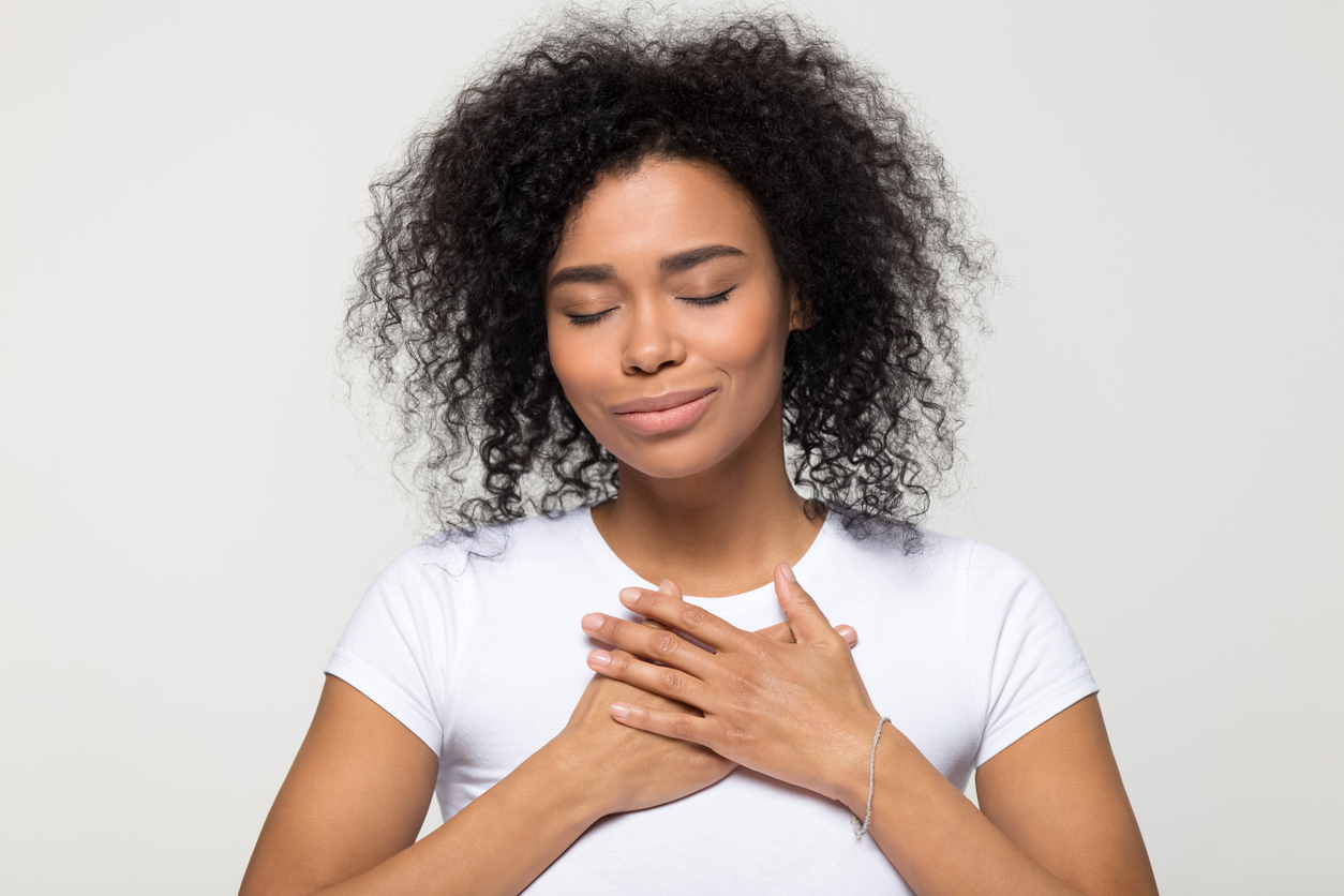 Grateful hopeful African American woman holding hands on chest Hopeful woman with hands over her heart